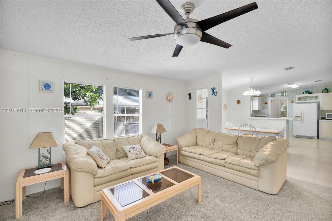 Living area featuring neutral carpeting, a central ceiling fan with integrated lighting, and multiple windows