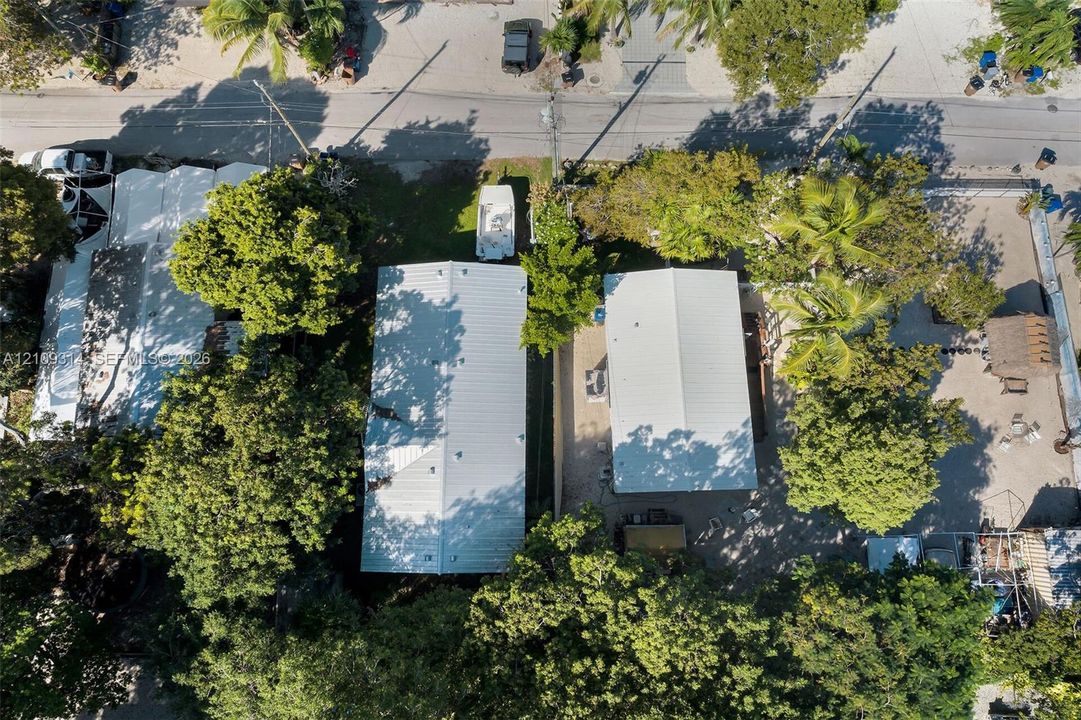 Aerial perspective featuring metal roof structures, mature tree canopy, and stone-surfaced outdoor areas