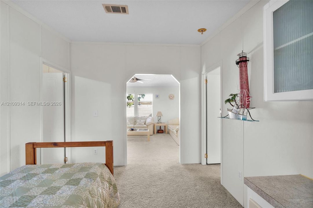 Interior space featuring neutral carpeting, a structural arched doorway, and a white built-in cabinet with glass-fronted doors and a stone-finish countertop
