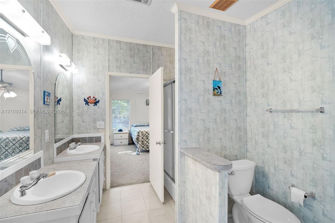 Dual vanity with oval drop-in sinks, tiled flooring, built-in shower enclosure, and designated toilet area separated by a partial wall