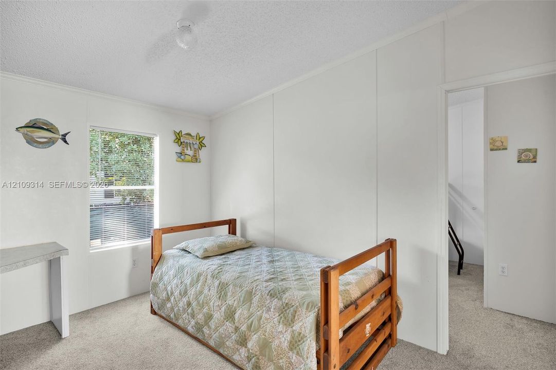 Neutral-toned interior space featuring white panel walls, carpeting, and a single window with natural light