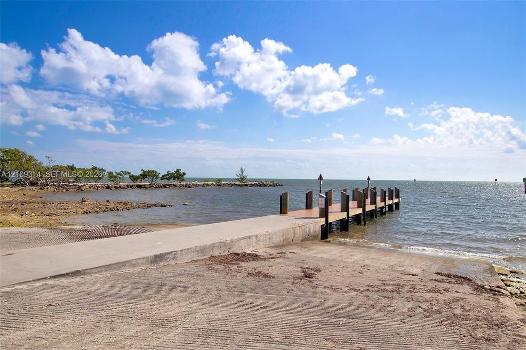 Concrete boat launch with a wooden dock featuring post lighting and pilings