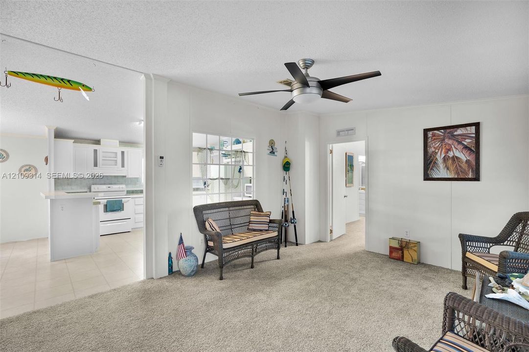Living area featuring neutral carpeting, a central ceiling fan with integrated lighting, and a grid-patterned window