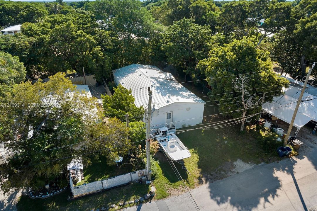 Aerial perspective featuring a detached structure with a metal roof, mature tree canopy, and landscaped grounds