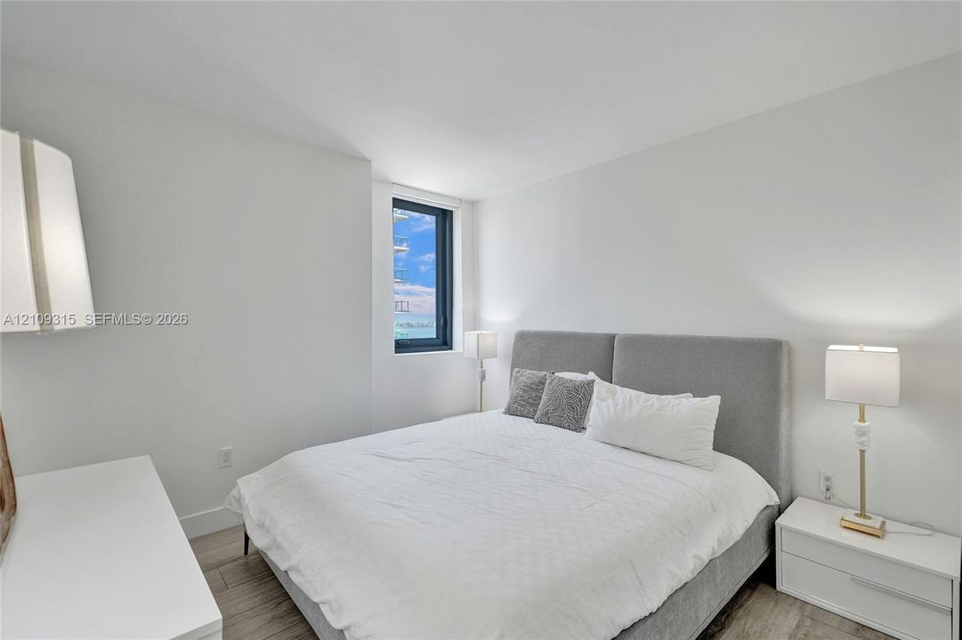 Neutral-toned room featuring wood-finish flooring, a tall vertical window, and crisp white wall finishes