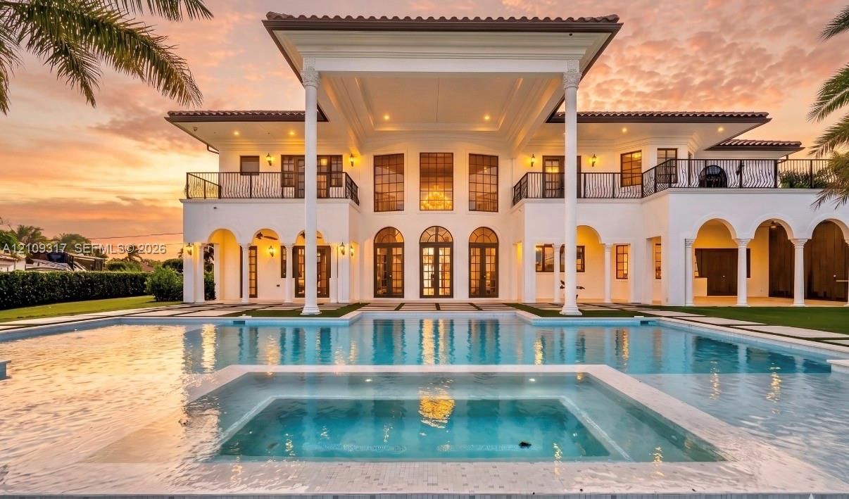 Two-story Mediterranean estate featuring arched colonnades, a second-level wrought iron balcony, custom multi-pane fenestration, and a ground-level swimming pool with an integrated spa