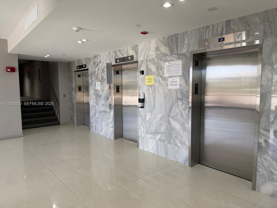 Elevator lobby featuring stone-clad wall accents, stainless steel elevator doors, recessed lighting, and polished flooring