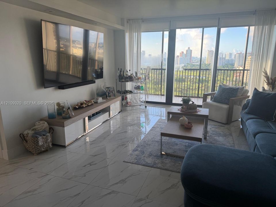 Large-format neutral flooring with veined detailing, floor-to-ceiling glass wall, and private balcony with an urban skyline backdrop