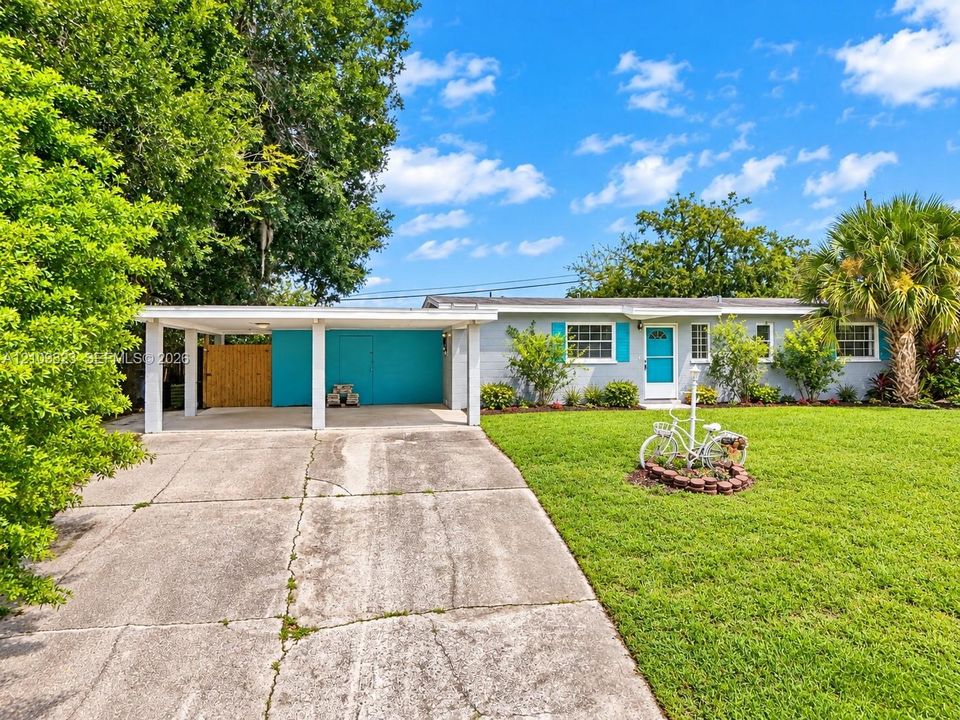 Single-story residence featuring a covered carport, concrete driveway, front lawn, and exterior shutters