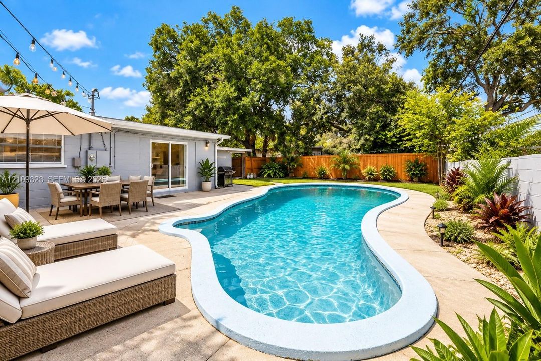 Backyard featuring a freeform swimming pool, expansive concrete decking, mature trees, and privacy fencing