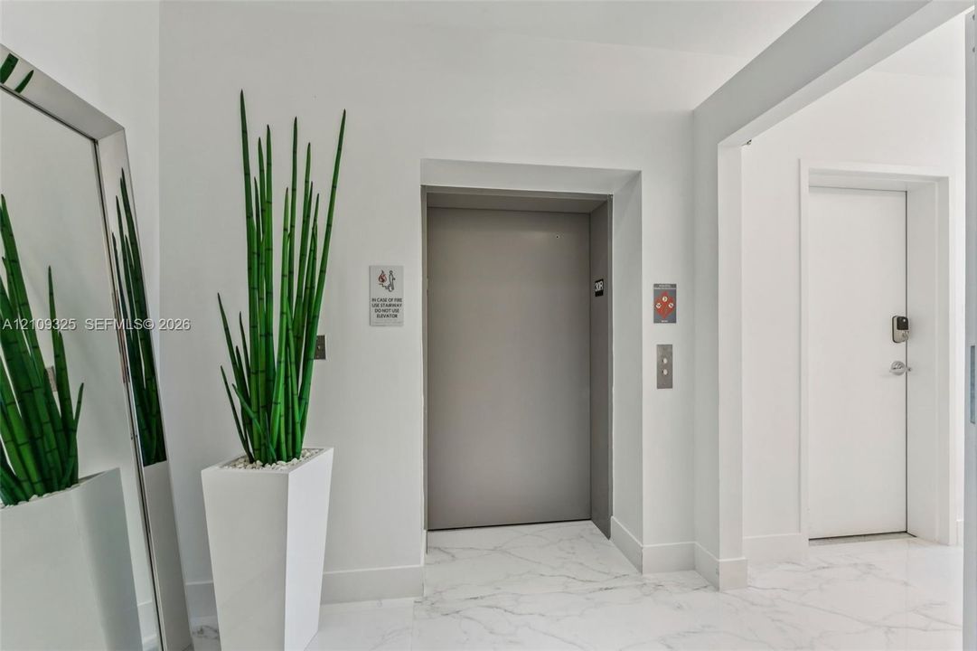 Private elevator access featuring a brushed metal control panel and neutral-toned doors, set within a hall finished with white stone-patterned flooring and smooth wall surfaces