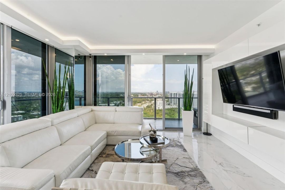 Floor-to-ceiling glass walls, integrated ceiling cove lighting, polished stone flooring, and expansive balcony access