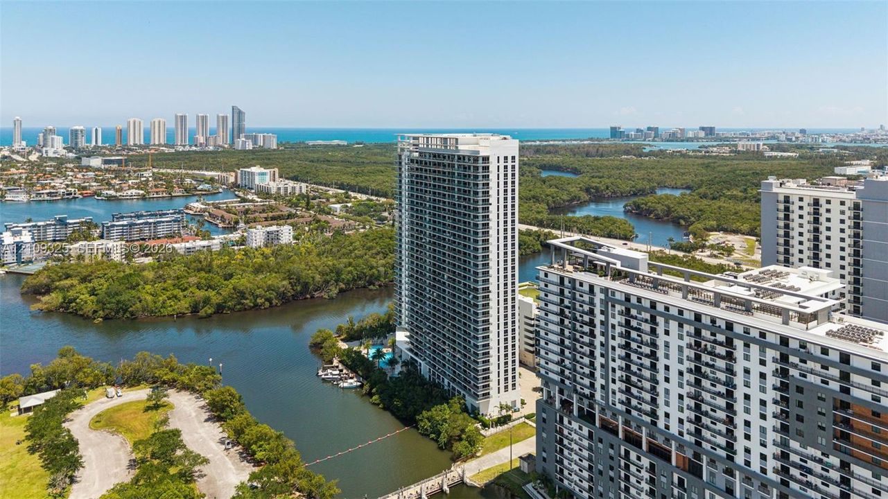 High-rise residential tower featuring balconies, extensive glass fenestration, and coastal surroundings with waterway access