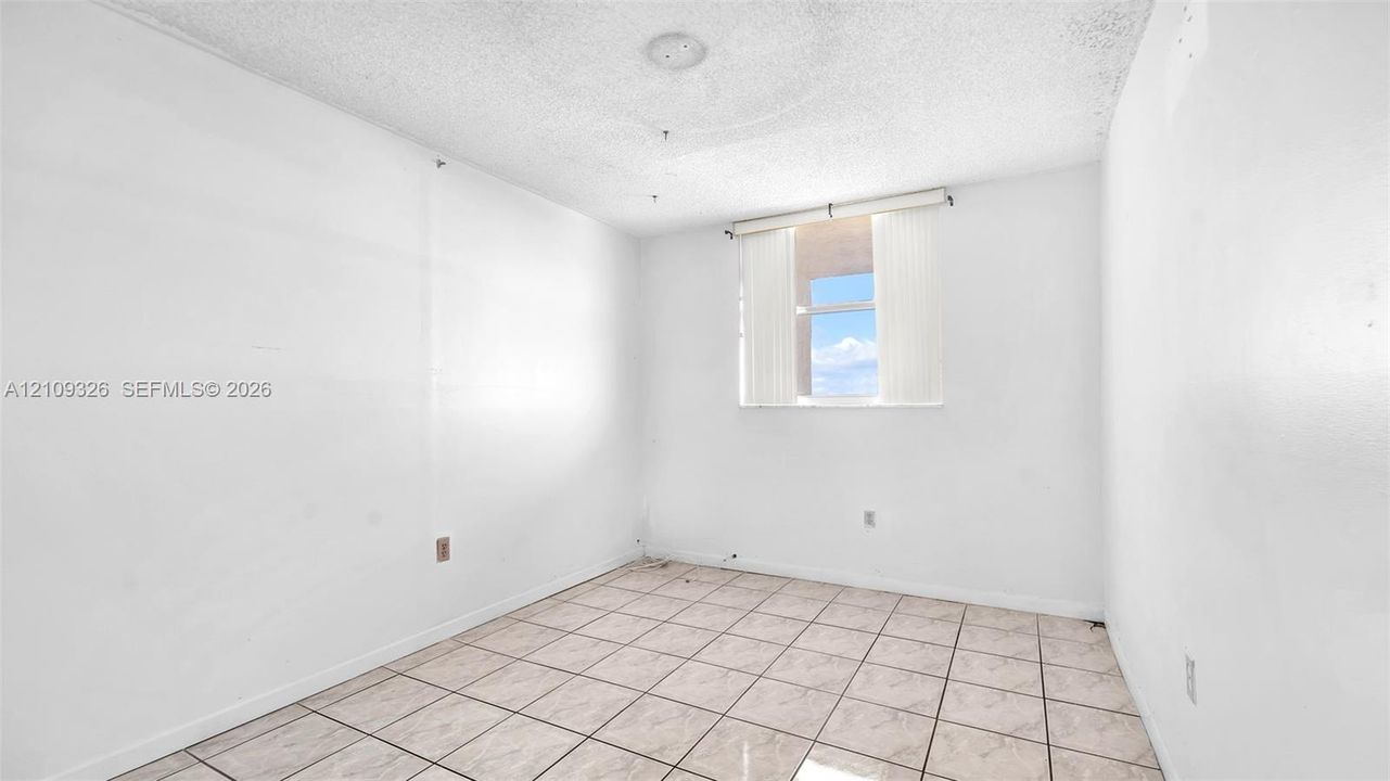 Interior room featuring ceramic tile flooring, neutral white walls, and a window with vertical blinds