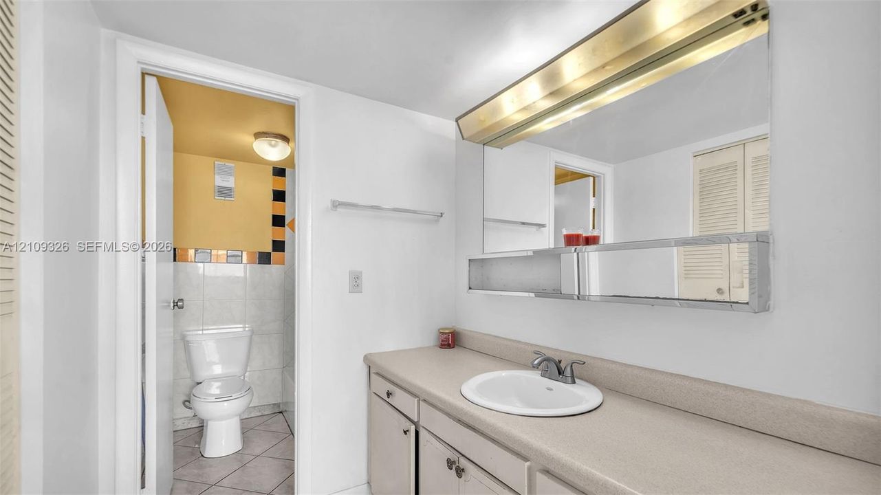 Bathroom featuring a vanity with a solid-surface countertop, an integrated sink, a full-width mirror with a built-in shelf, and a multi-light fixture
