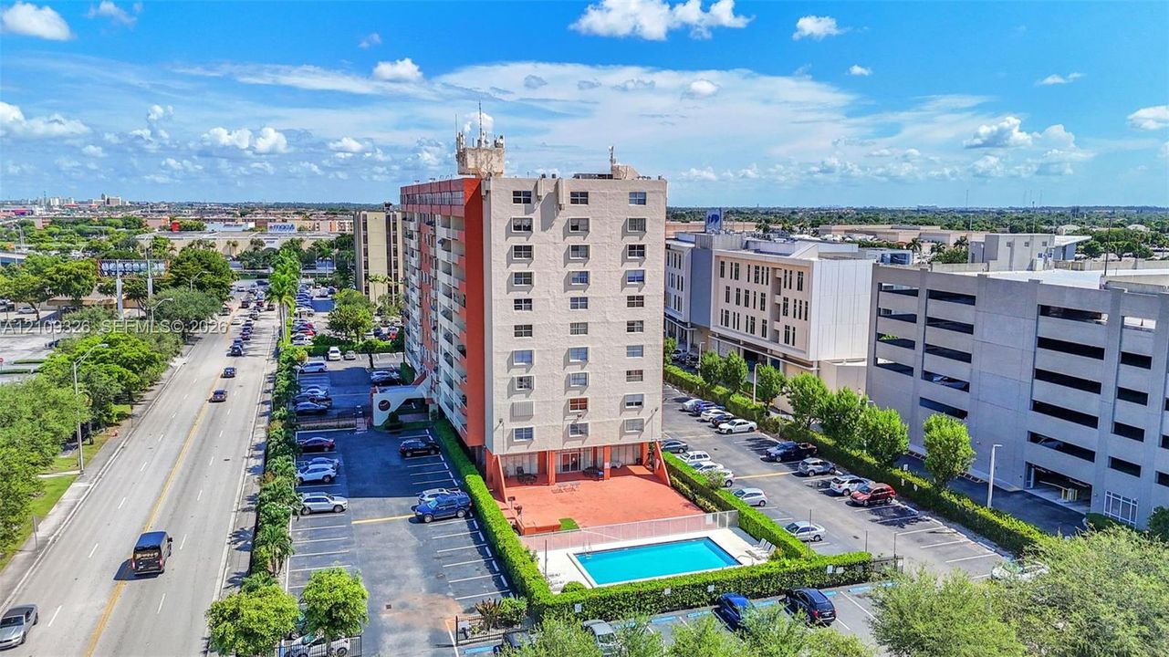 Multi-story residential building featuring an exterior pool, ground-level paved courtyard, designated surface parking, and manicured perimeter landscaping