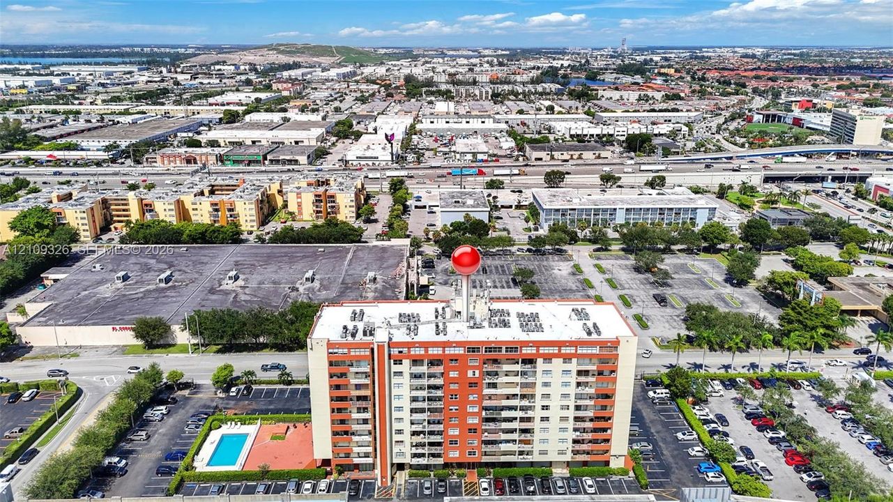 Multi-story residential building featuring exterior balconies, a paved surface parking lot, and an outdoor swimming pool with a surrounding deck