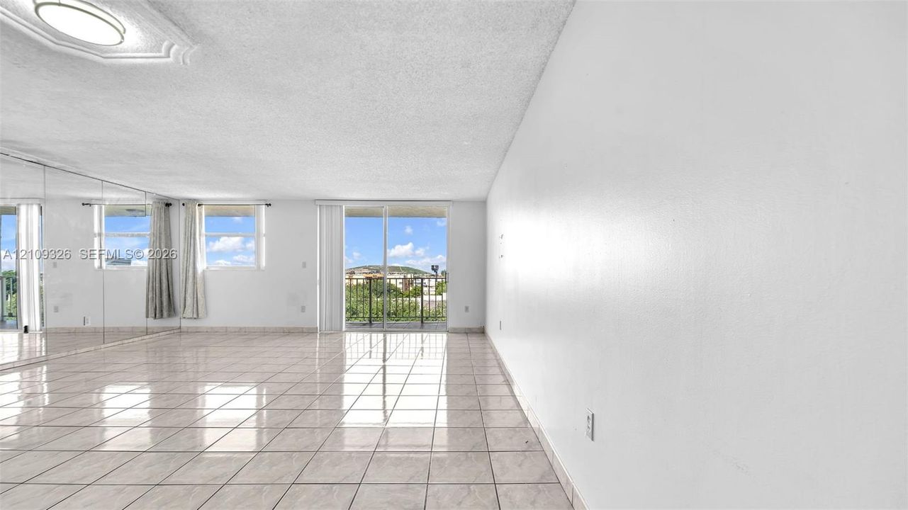 Open-concept living space featuring high-gloss tile flooring, floor-to-ceiling wall mirrors, recessed ceiling lighting, and sliding glass doors with balcony access