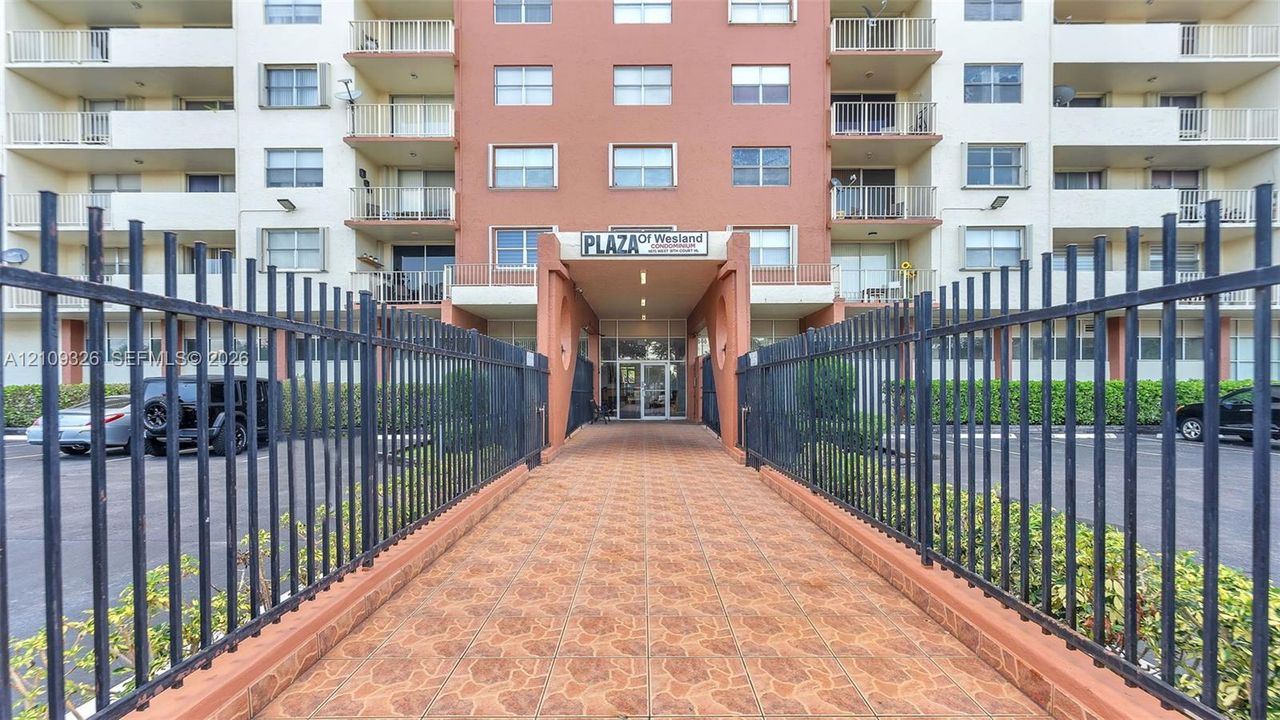 Multi-story exterior featuring masonry construction, private balconies with railings, and a tiled walkway entry path flanked by decorative metal fencing