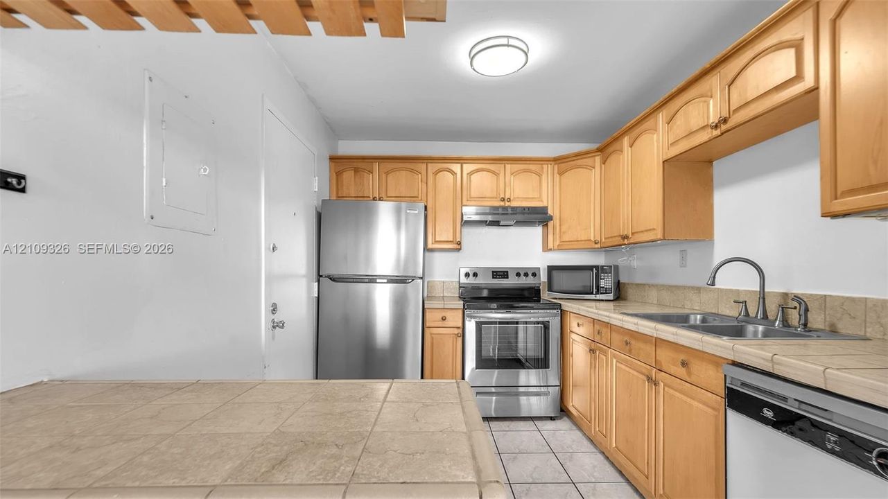 Kitchen featuring light-finish wood cabinetry, stainless steel appliances, tile countertops, and ceramic tile flooring