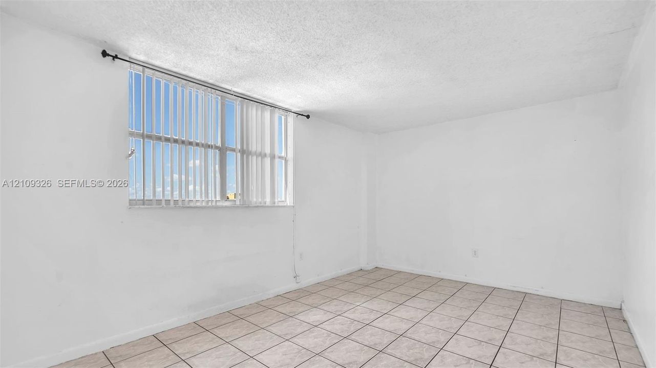 Interior room featuring neutral wall finishes, ceramic tile flooring, and a large window with vertical blinds