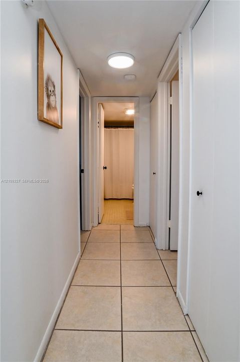 Hallway featuring neutral-toned tile flooring, flush-mount lighting, and multiple interior doors