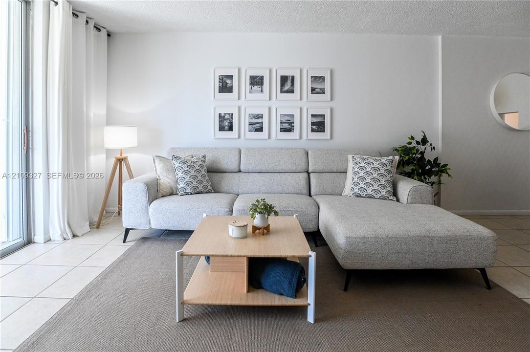 Living space featuring large format light-toned floor tiling, textured ceiling, and sliding glass door with full-height window panels