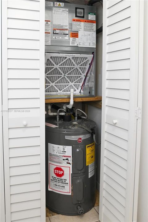 Utility closet featuring white bi-fold doors, a vertical air handler unit, and a tank-style water heater