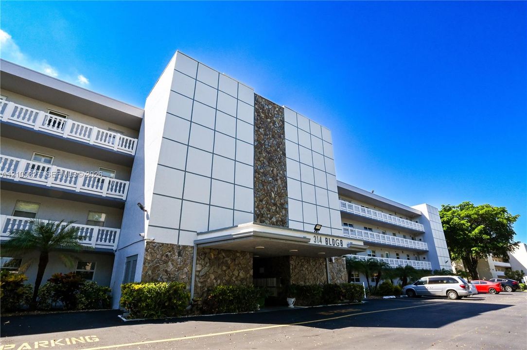 Mid-rise building exterior featuring a panelized façade, stone masonry detailing, a covered entrance, and tiered private balconies with white railings