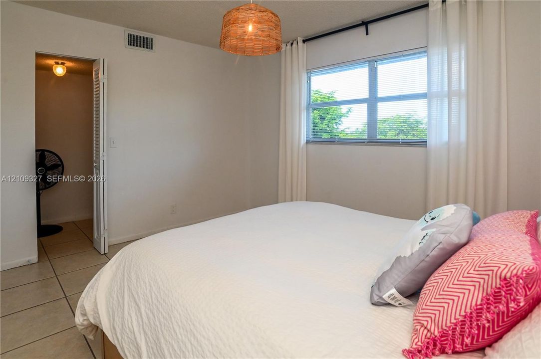 Neutral-toned room featuring ceramic tile flooring, a large window, a woven-texture hanging light fixture, and a louvered-door closet