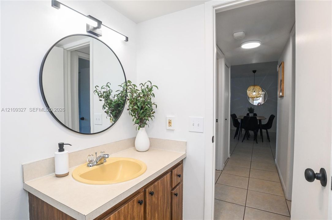 Vanity featuring wood-finish cabinetry, a neutral countertop, an integrated sink, and a circular wall-mounted mirror with integrated lighting