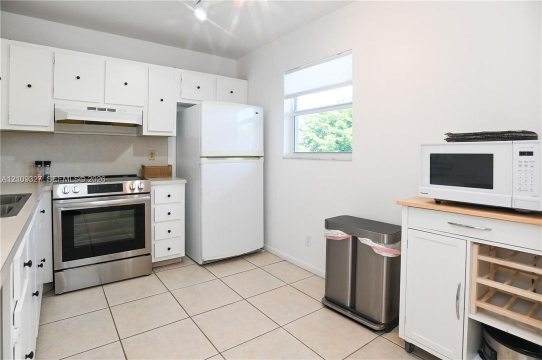 Kitchen featuring white cabinetry, stainless steel range, tile flooring, and neutral solid-surface countertops