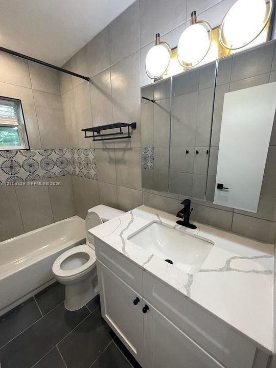 White cabinetry vanity with a stone-composite countertop, matte black faucet, wall-mounted medicine cabinet with integrated lighting, and decorative tile accent wall