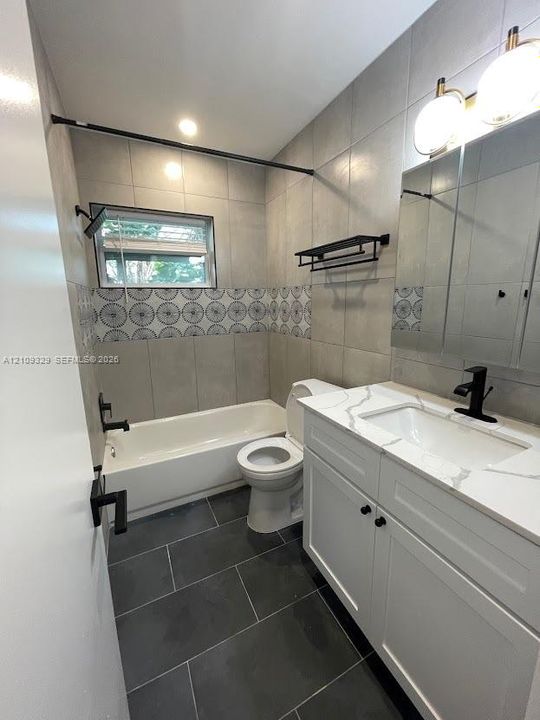 Bathroom featuring a stone-surface vanity with a rectangular sink, matte black fixtures, large-format grey tile flooring, patterned decorative wall tile, and a built-in medicine cabinet