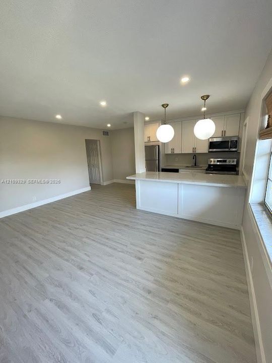 Kitchen featuring white cabinetry, a breakfast bar with stone-finish countertop, recessed lighting, and dual globe pendant lights, complemented by wood-finish flooring