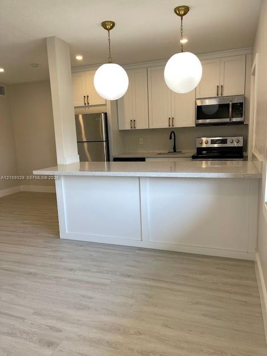 Kitchen featuring white cabinetry, a stone-composite countertop, wood-finish flooring, stainless steel appliances, and dual globe pendant lighting