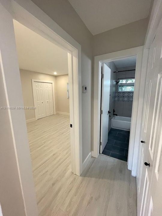 Wood-finish flooring throughout, light-toned interior walls, dual-panel interior doors, and a bathroom featuring dark-toned floor tiling and decorative tile wall accents