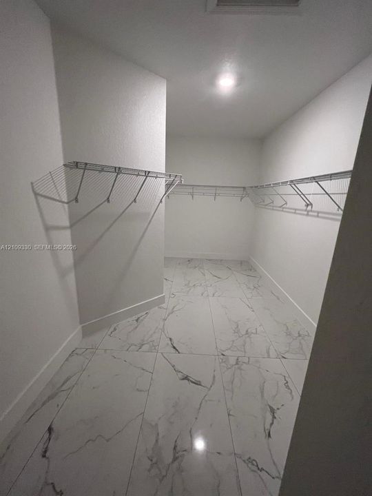 Walk-in closet featuring large-format tile flooring with a neutral veined pattern, white walls, and tiered metal wire shelving