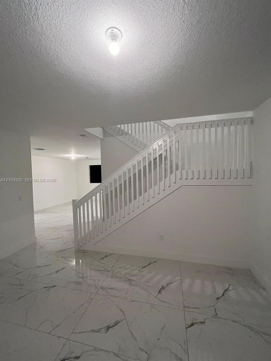 Large-format tile flooring with a neutral veined pattern, open staircase with white vertical balusters, and flush-mount ceiling lighting