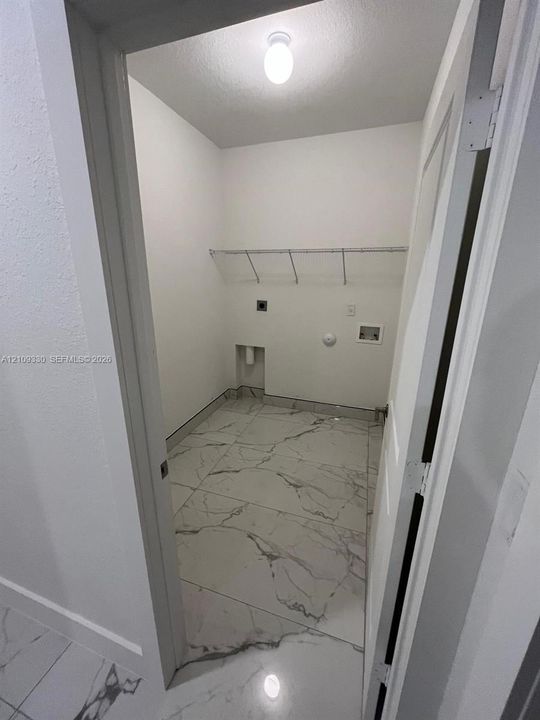 Utility space featuring large-format tile flooring with a neutral veining pattern, built-in wire shelving, and dedicated washer and dryer hookups