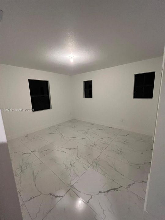 Room featuring large-format white stone-finish flooring with dark grey veining, crisp neutral wall paint, and three windows
