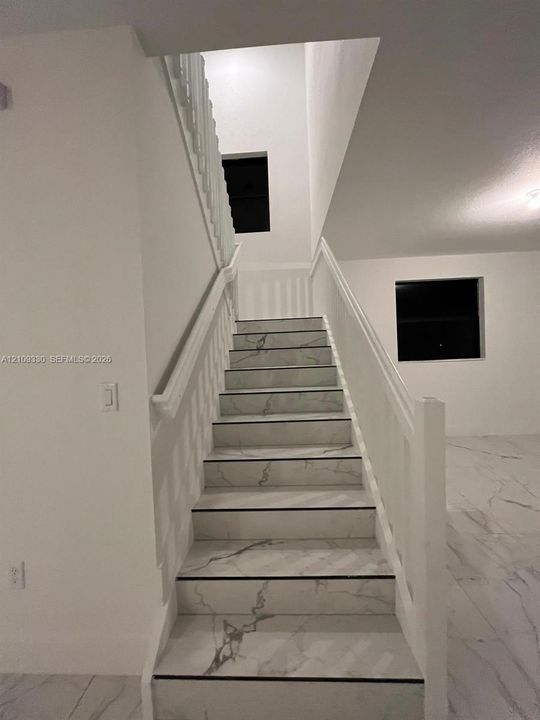Staircase featuring white stone-finish treads with grey veining, a painted white handrail, and white balusters