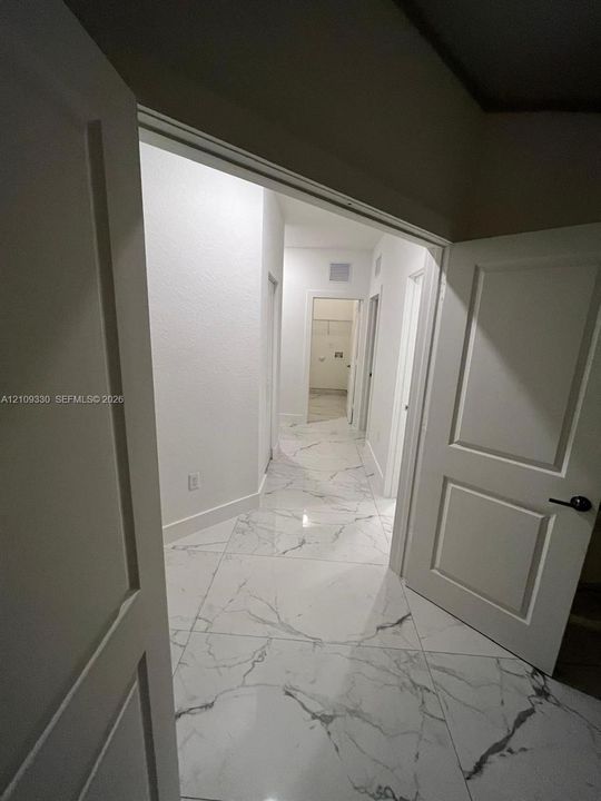 Hallway featuring large-format tile flooring with a veined stone pattern, solid-core interior doors, and crisp white walls