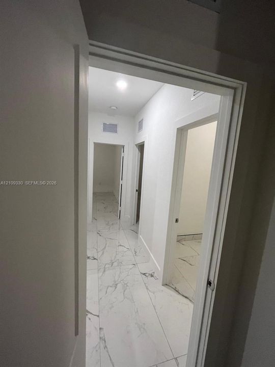 Hallway featuring large-format tile flooring with veining detail, recessed lighting, and white door frames