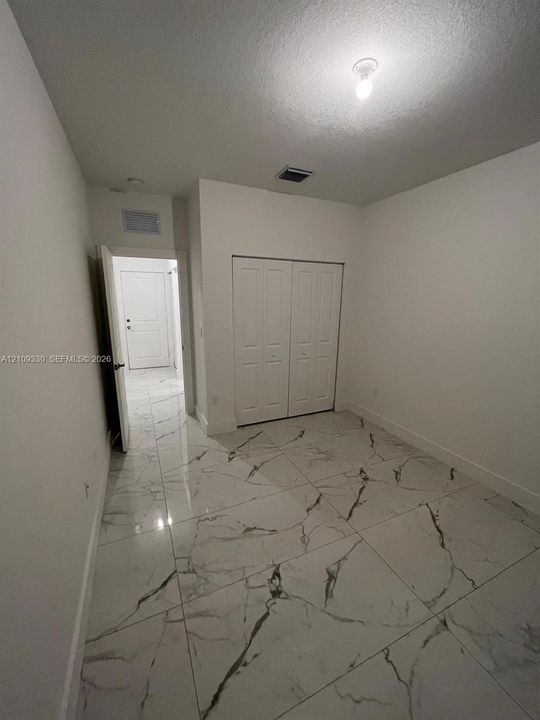 Large-format tile flooring with a veined pattern, neutral wall palette, and double-door reach-in closet