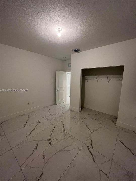 Interior room featuring large-format stone-patterned floor tile, a recessed walk-in closet with integrated shelving, and a paneled interior door