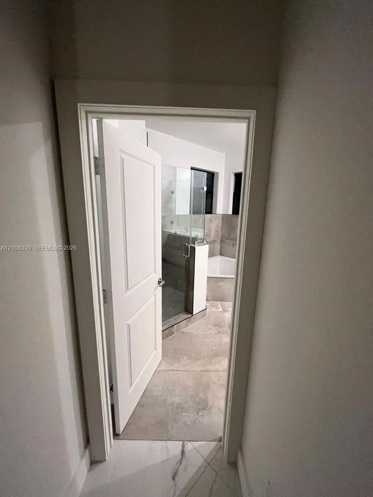 Bathroom interior featuring large-format tile flooring, a glass-enclosed shower, a soaking tub, and a multi-panel door