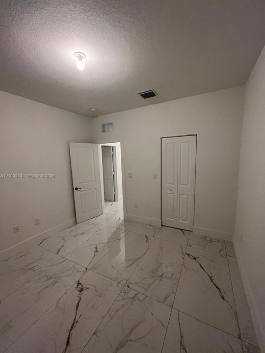 Large-format stone-patterned tile flooring, neutral wall finishes, white six-panel interior doors, and a double-door closet