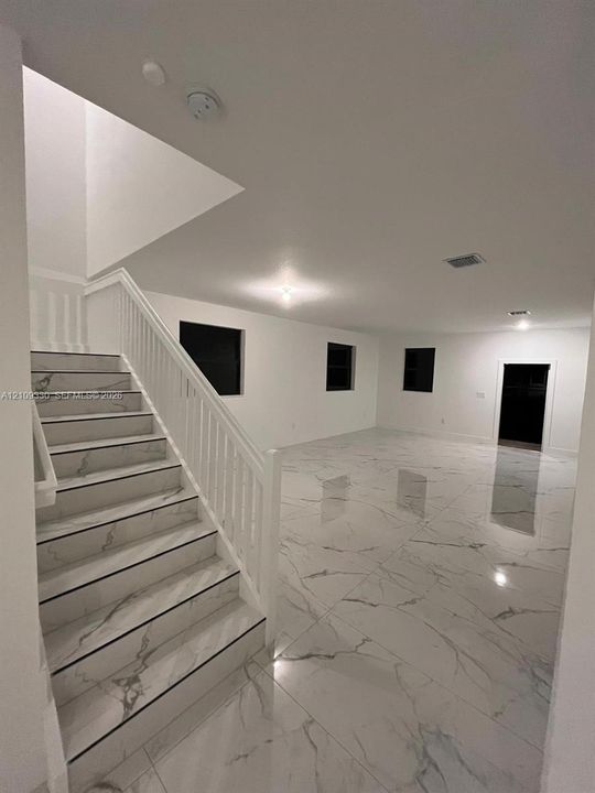Large-format stone-finish flooring with veining detail and staircase featuring matching stone-finish treads, white balustrades, and handrail