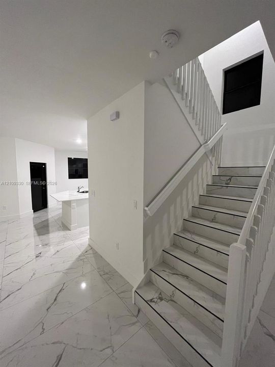 Staircase featuring white balusters and stone-finish treads, complemented by extensive stone-finish floor tiling and a kitchen island with a stone-finish countertop